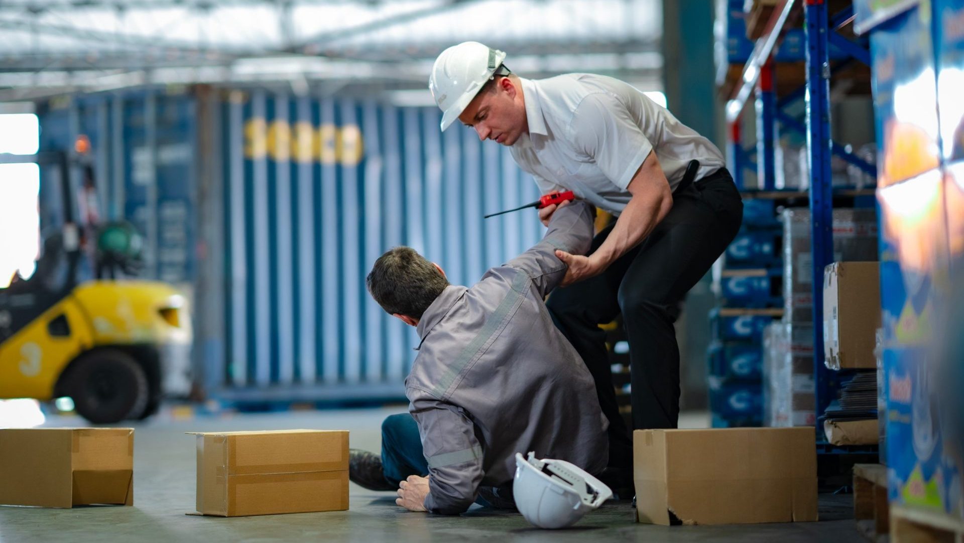 Young worker rushes to help injured senior colleague who fell in warehouse. Team support, safety response, and workplace accident awareness.