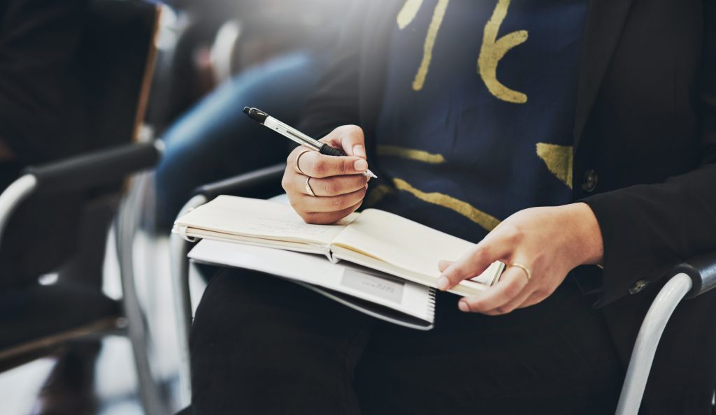 Businessperson sits in a chair writing in a notebook in workplace seminar for learning or upskill