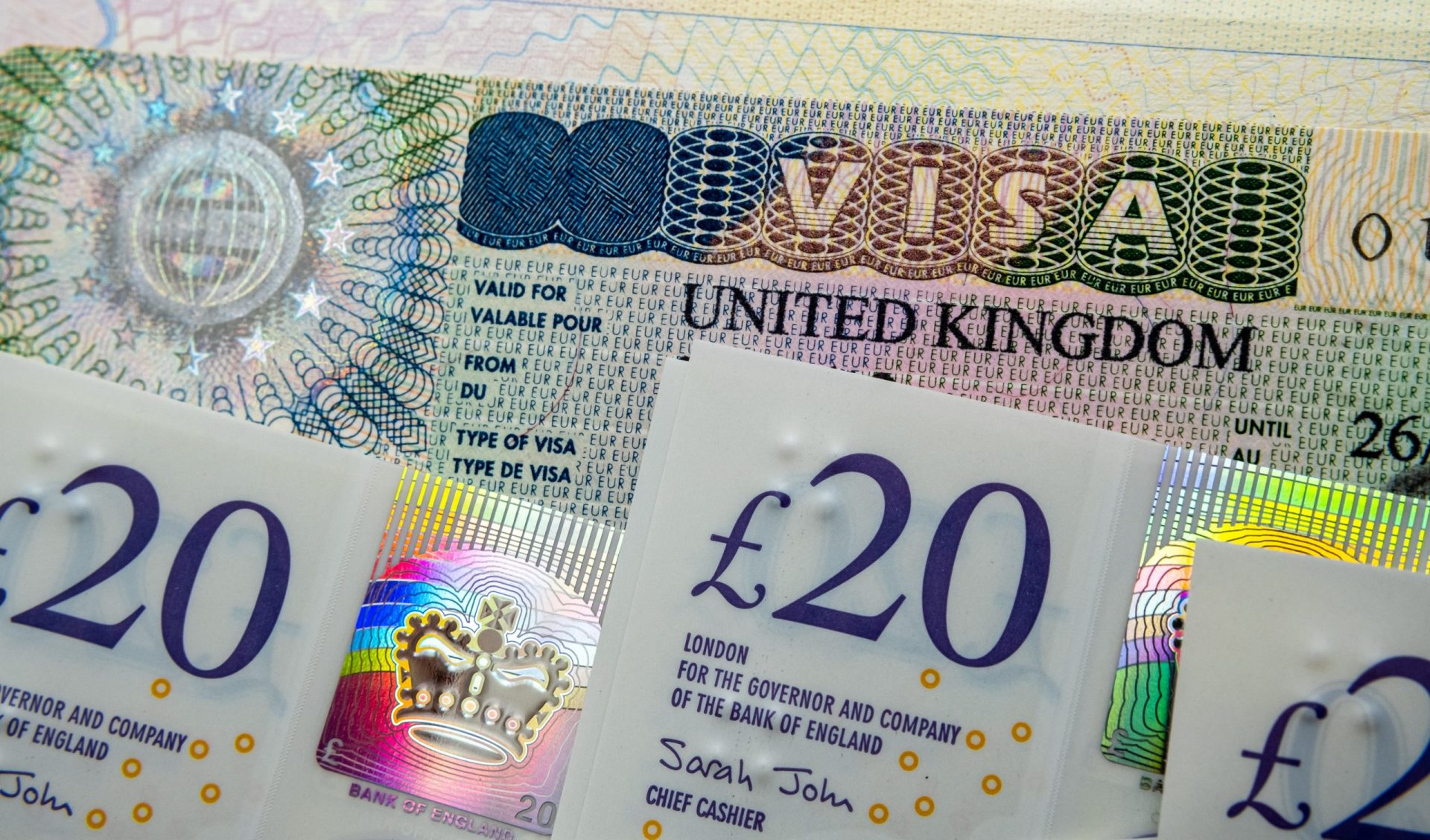 UK entry business and tourist visa in passport and pile of 20 pound banknotes.