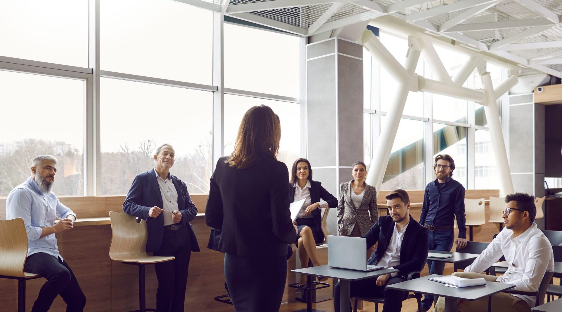 a speaker presents to a group of businesspeople spaced casually around a room.