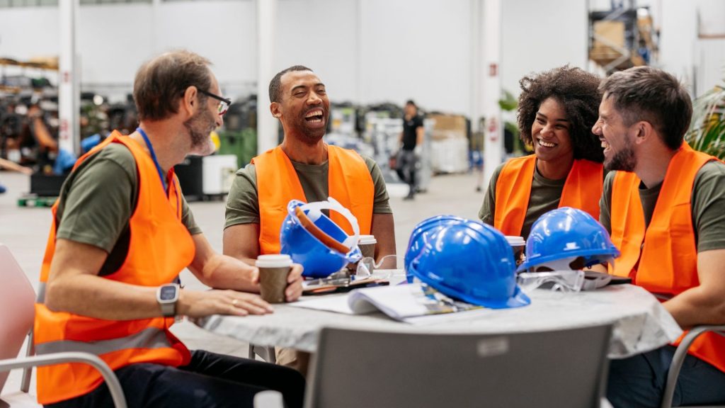 A group of engineers in high visibility vests happily chat during a break at a table.